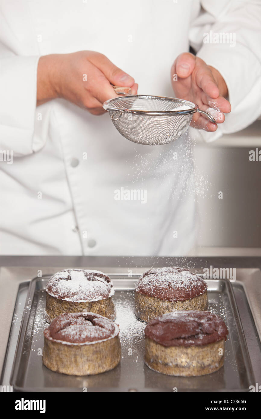 Mid- adult chef sieves icing sugar over chocolate cakes Stock Photo