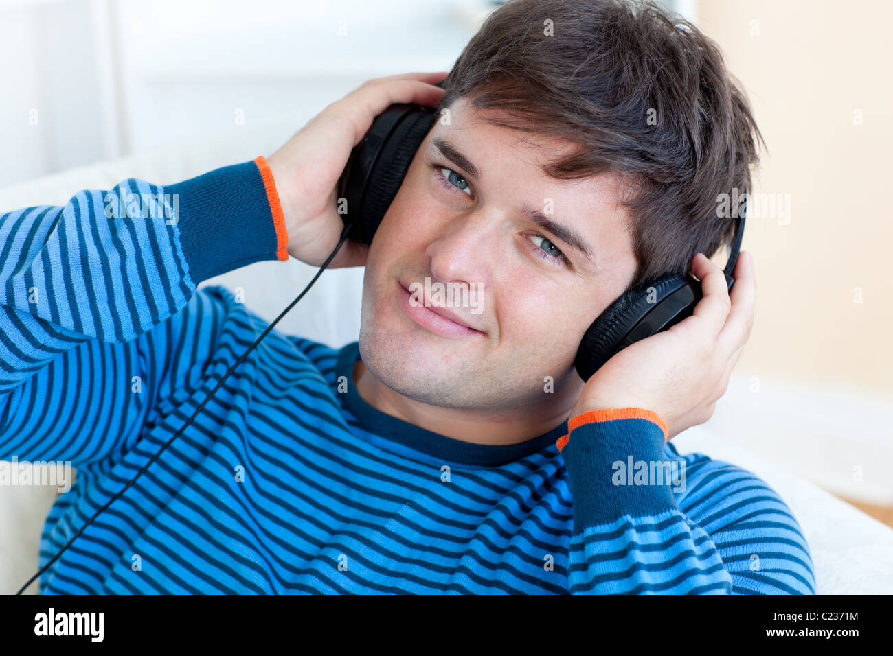 Cheerful man listening music with headphones on lying in the living-room Stock Photo