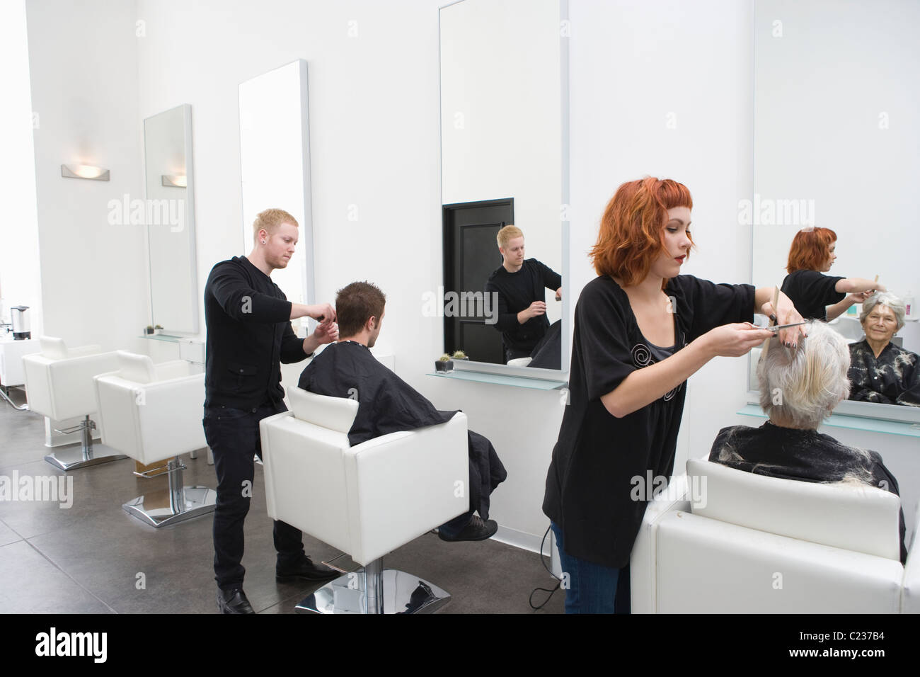 Stylists cut clients' hair in unisex salon Stock Photo