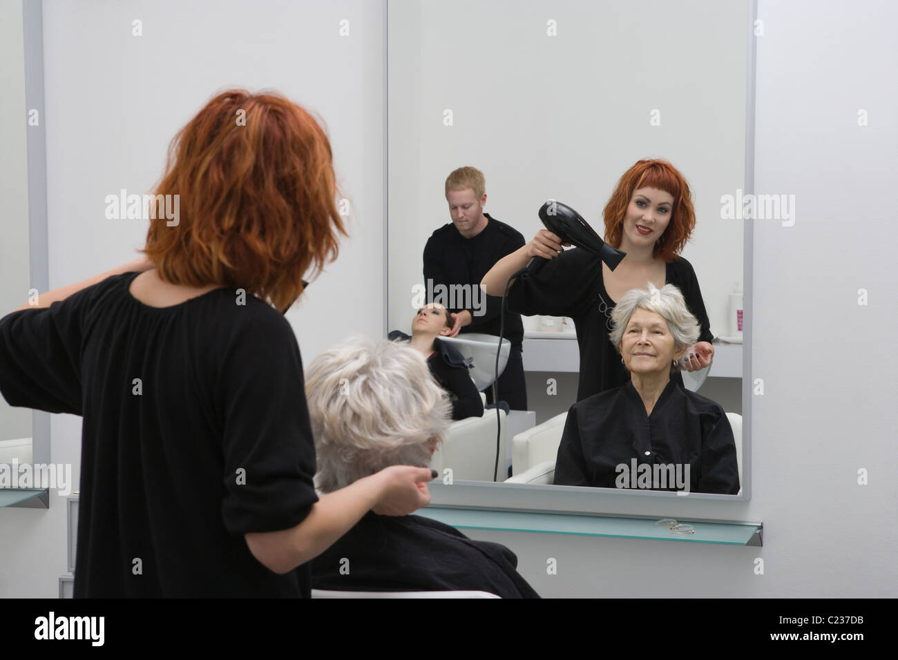 Stylist blow-drys elderly woman's hair Stock Photo