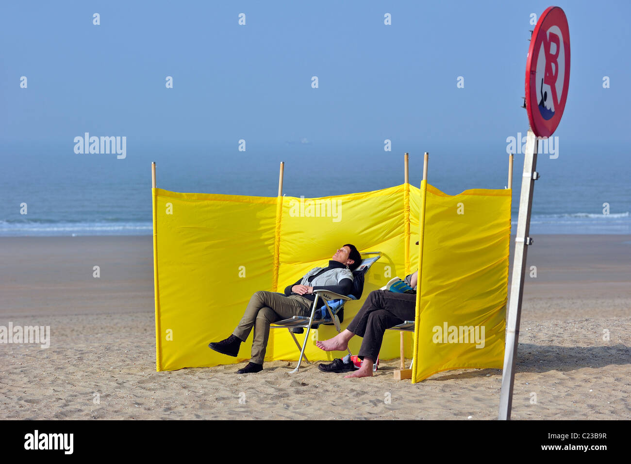 Tourists sunbathing behind windbreak on beach during early spring, Ostend, Belgium Stock Photo