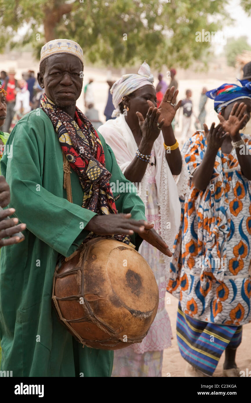 A man plays a calabash drum as women dance and clap during the FECHIBA horse festival in Barani, Burkina Faso Stock Photo