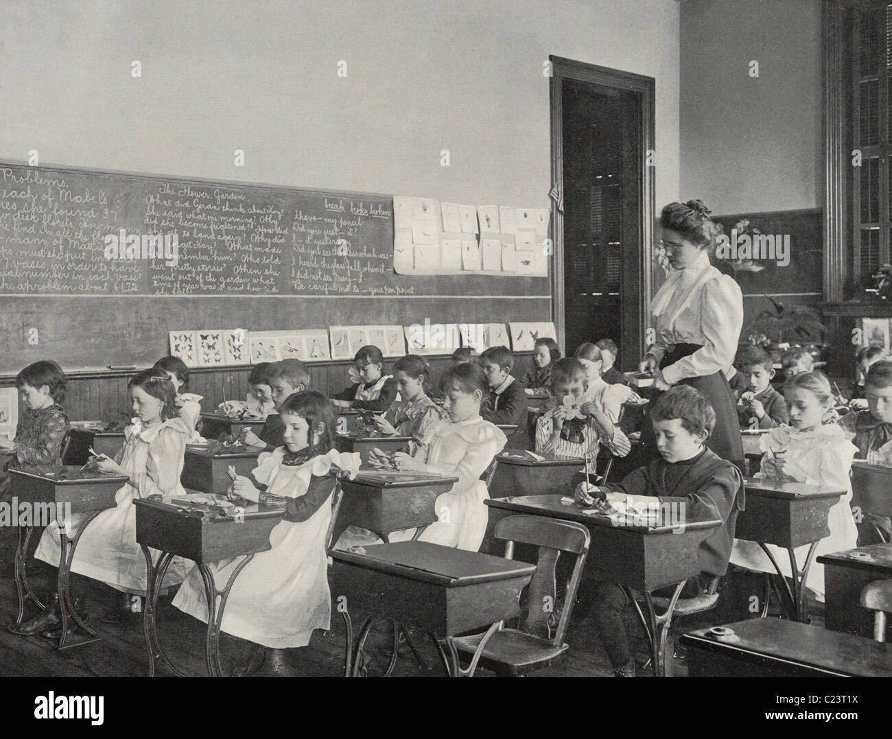 Historic photo of a group of Victorian Era school children cutting paper into leaf shapes, as their teacher looks on. Stock Photo