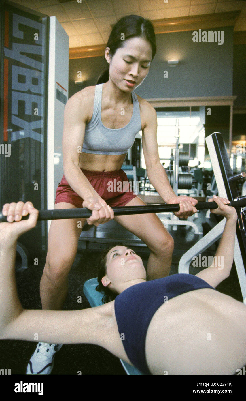 Woman spotting for another woman at the gym. Stock Photo