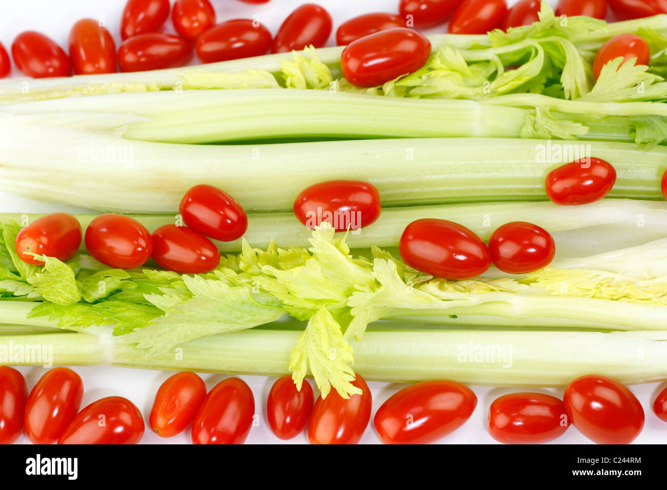 Organic celery heart stalks with small cherry plum tomatoes on a white background. Fresh long green vegetable and small round red fruit mix on white. Stock Photo