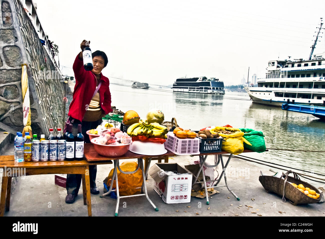 CHINA, SANDOUPING: Female vendor selling wine, beer and fresh fruits to tourists from the cruise ships that stop at Sandouping Stock Photo