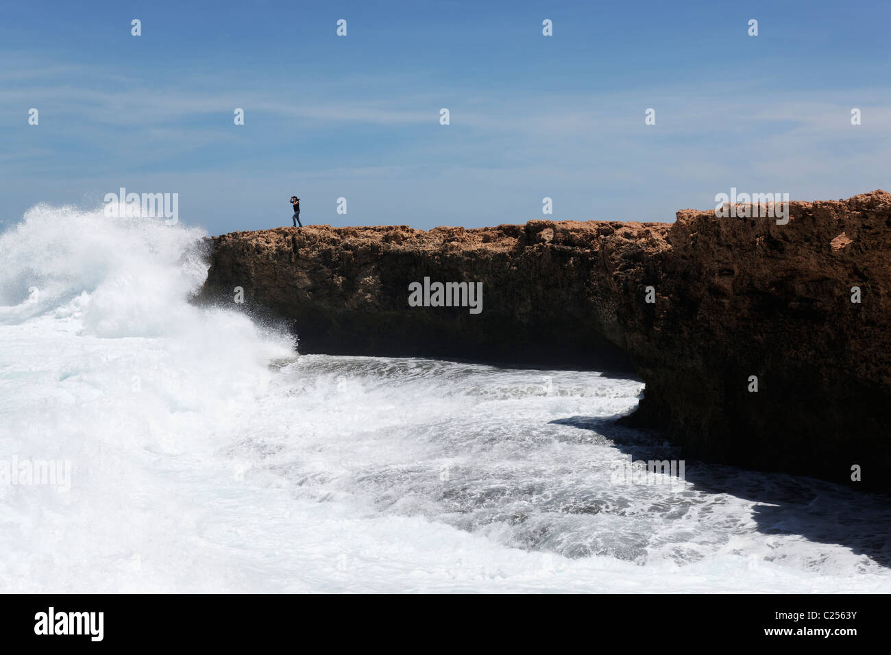 Woman standing on cliff as waves break along coastline, Quobba Western Australia Stock Photo