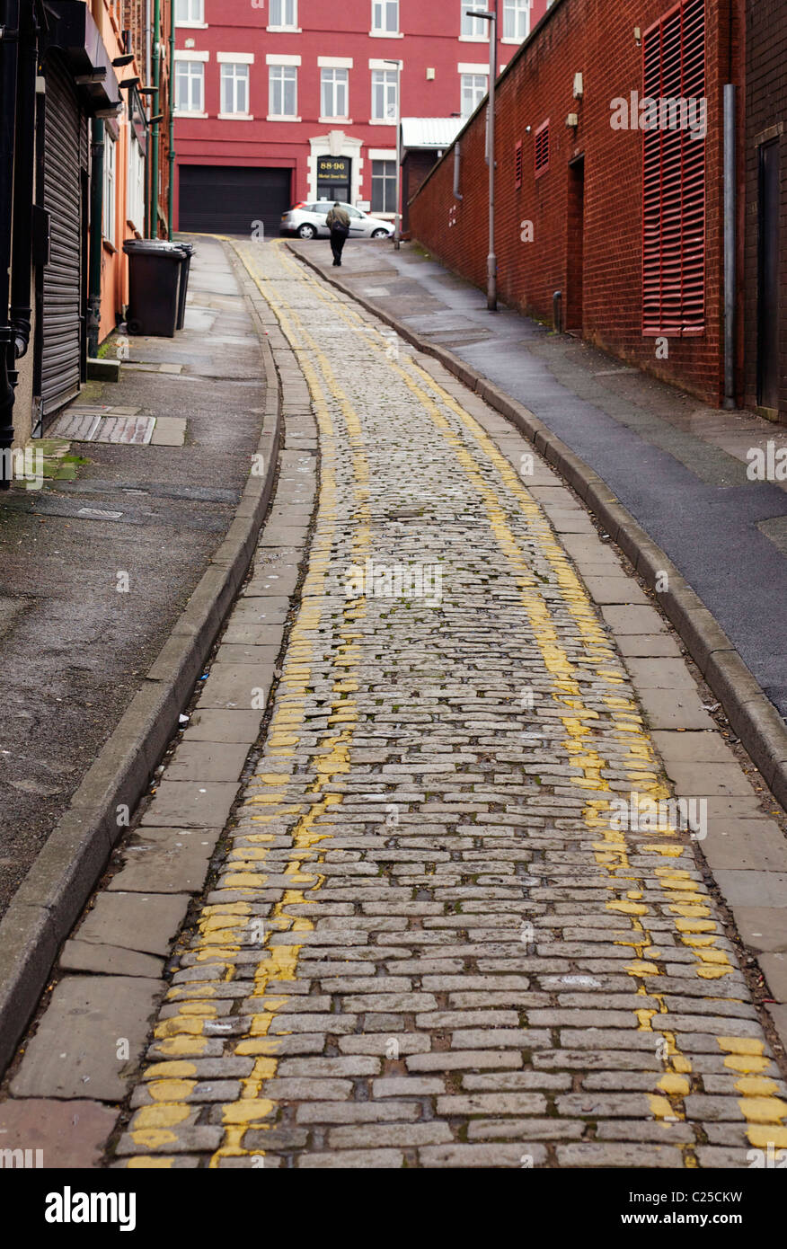 Man walking up a hilly cobbled narrow street with double yellow lines ...