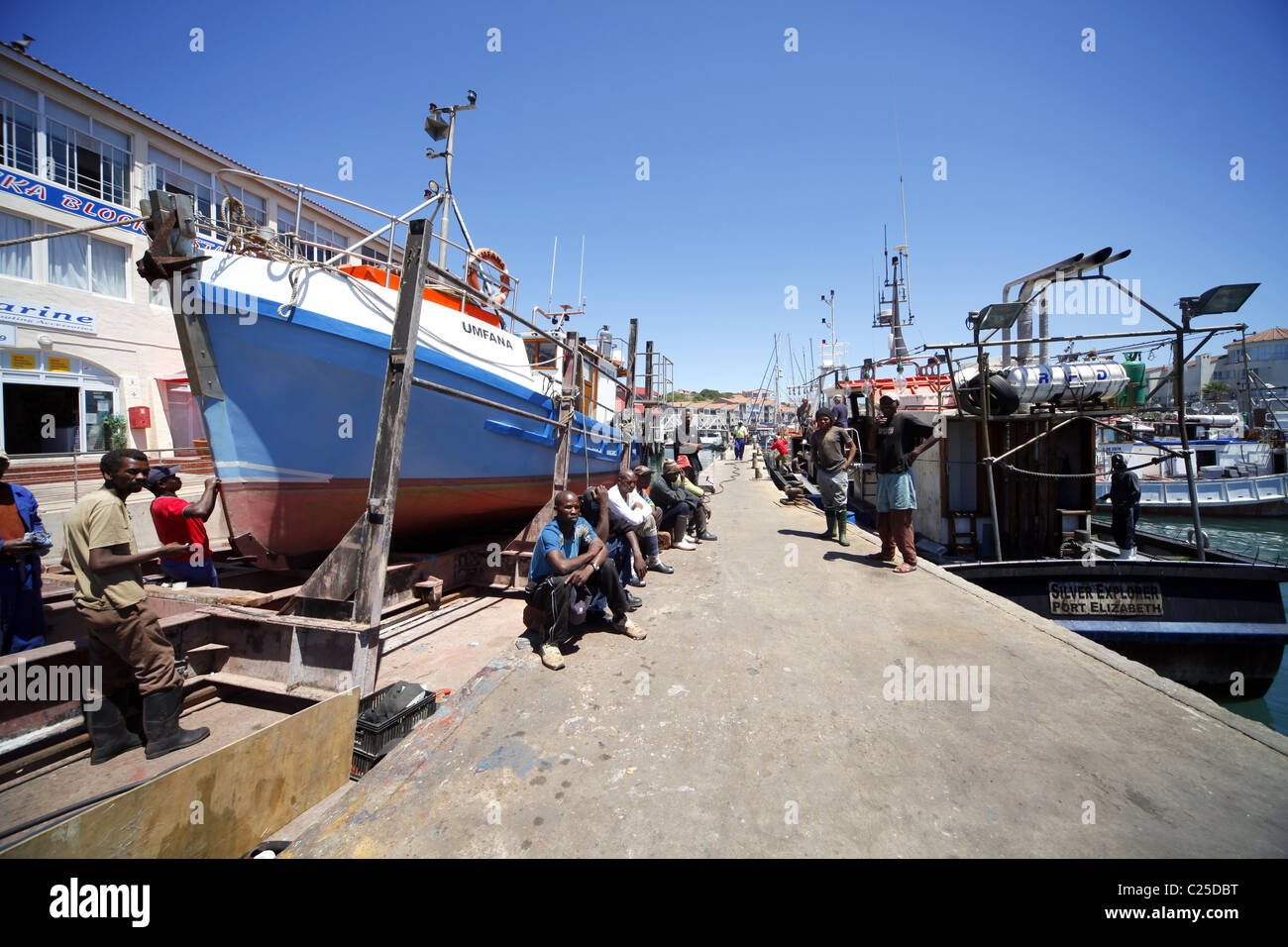 BLACK COLOURED WORKERS SIT NEAR FISHING BOAT ST. FRANCIS HARBOUR