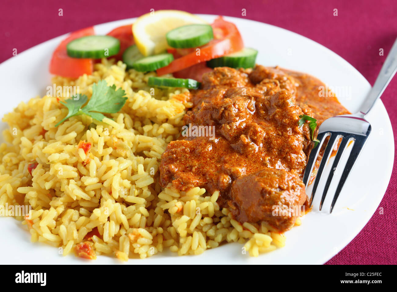 A meal of Kashmiri lamb curry with rice and salad on a maroon