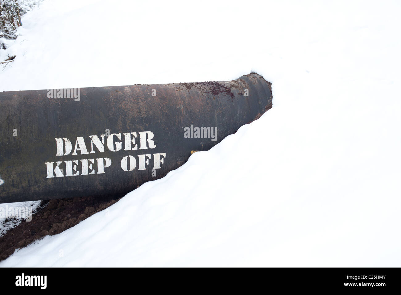 black pipe running into a bank of snow.  Writing on pipe reads danger keep off Stock Photo