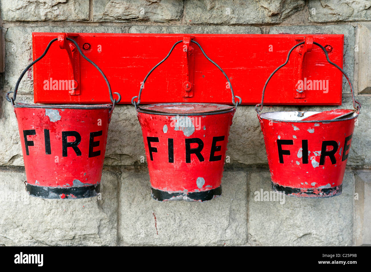Row of three old red fire buckets hanging from a wall Stock Photo