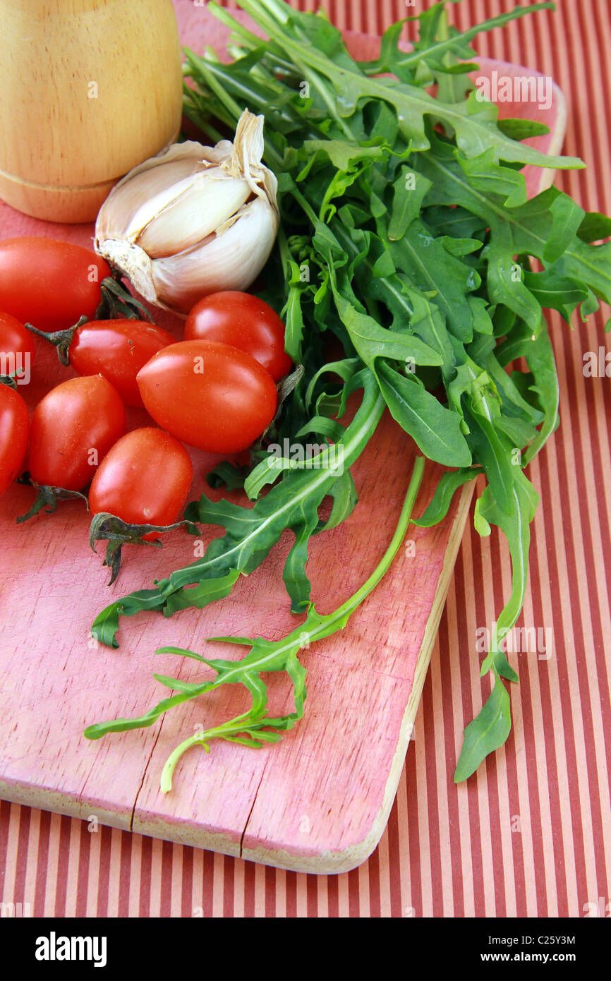 Bunch of fresh arugula with garlic and tomato on a cutting board Stock Photo