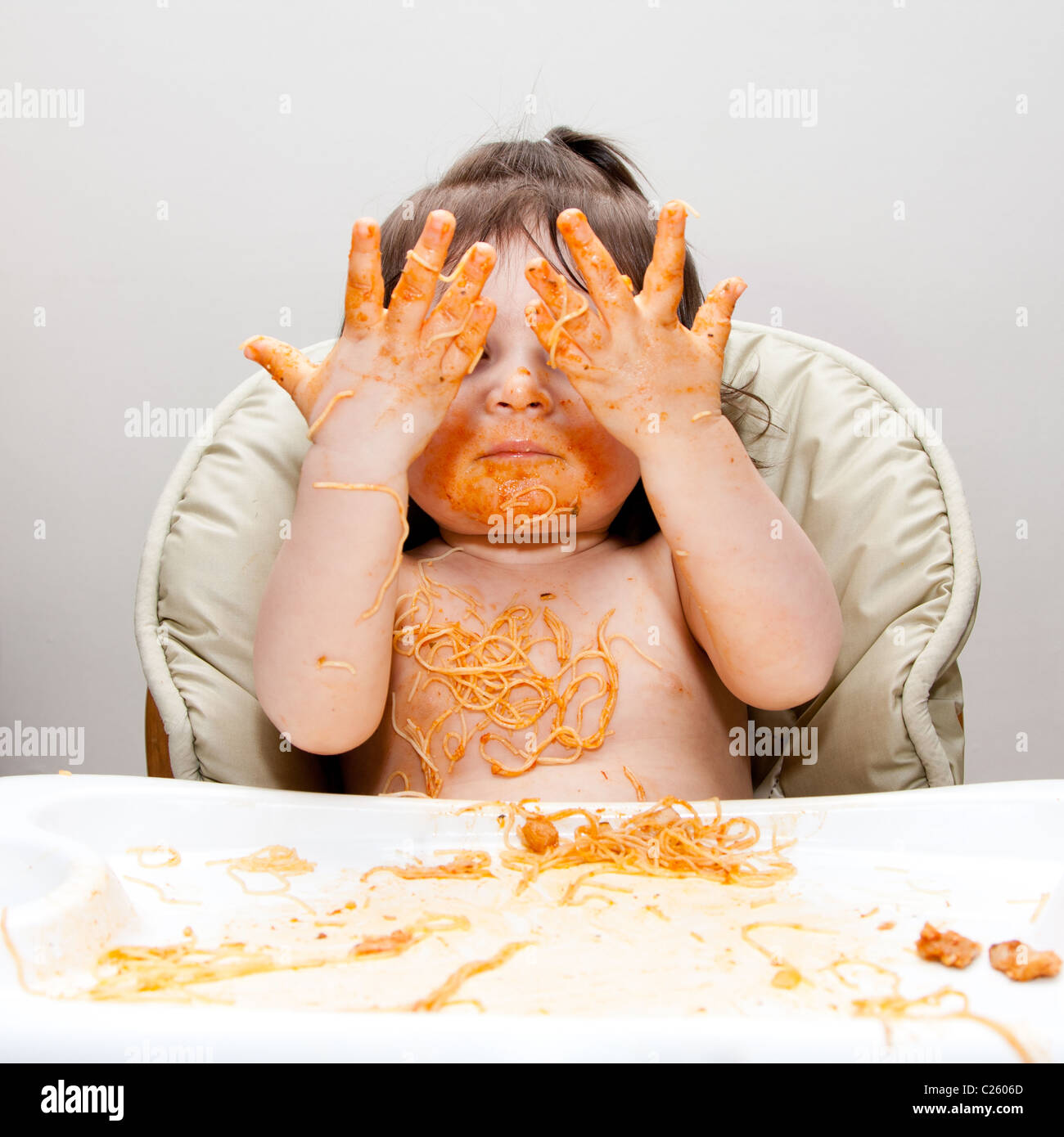 Happy baby having fun eating messy showing hands covered in Spaghetti Angel Hair Pasta red marinara tomato sauce. Stock Photo