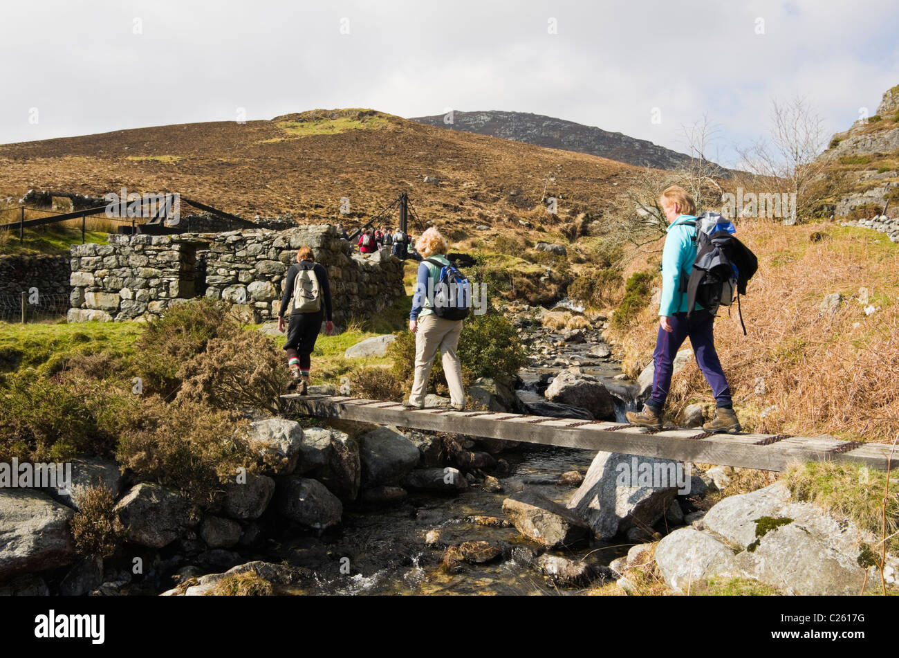 Walkers crossing footbridge over a stream by 19th century Cwm Ciprwth