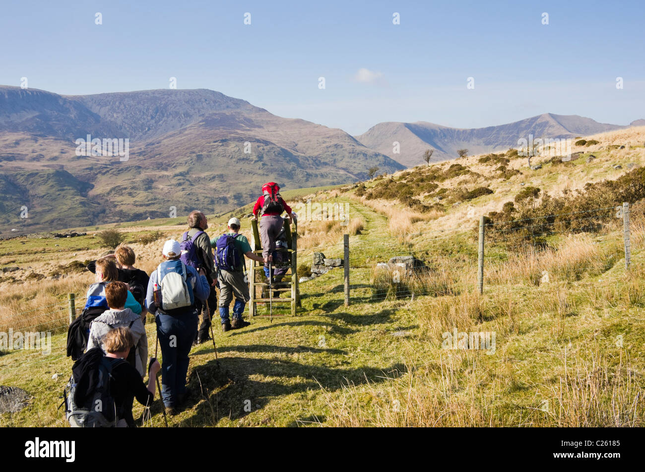 Group of Ramblers climbing over a stile on path in Cwm Pennant in Snowdonia National Park North Wales UK Britain Stock Photo