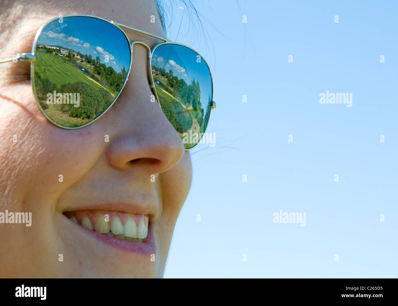 A smiling young woman wearing sunglasses that reflect the layout of an ...