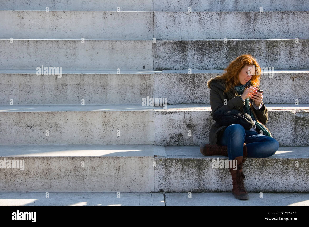 Young woman sat on concrete steps using a mobile telephone. Stock Photo