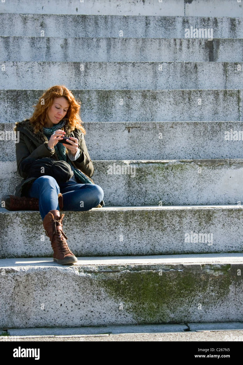 Young woman sat on concrete steps using a mobile telephone. Stock Photo