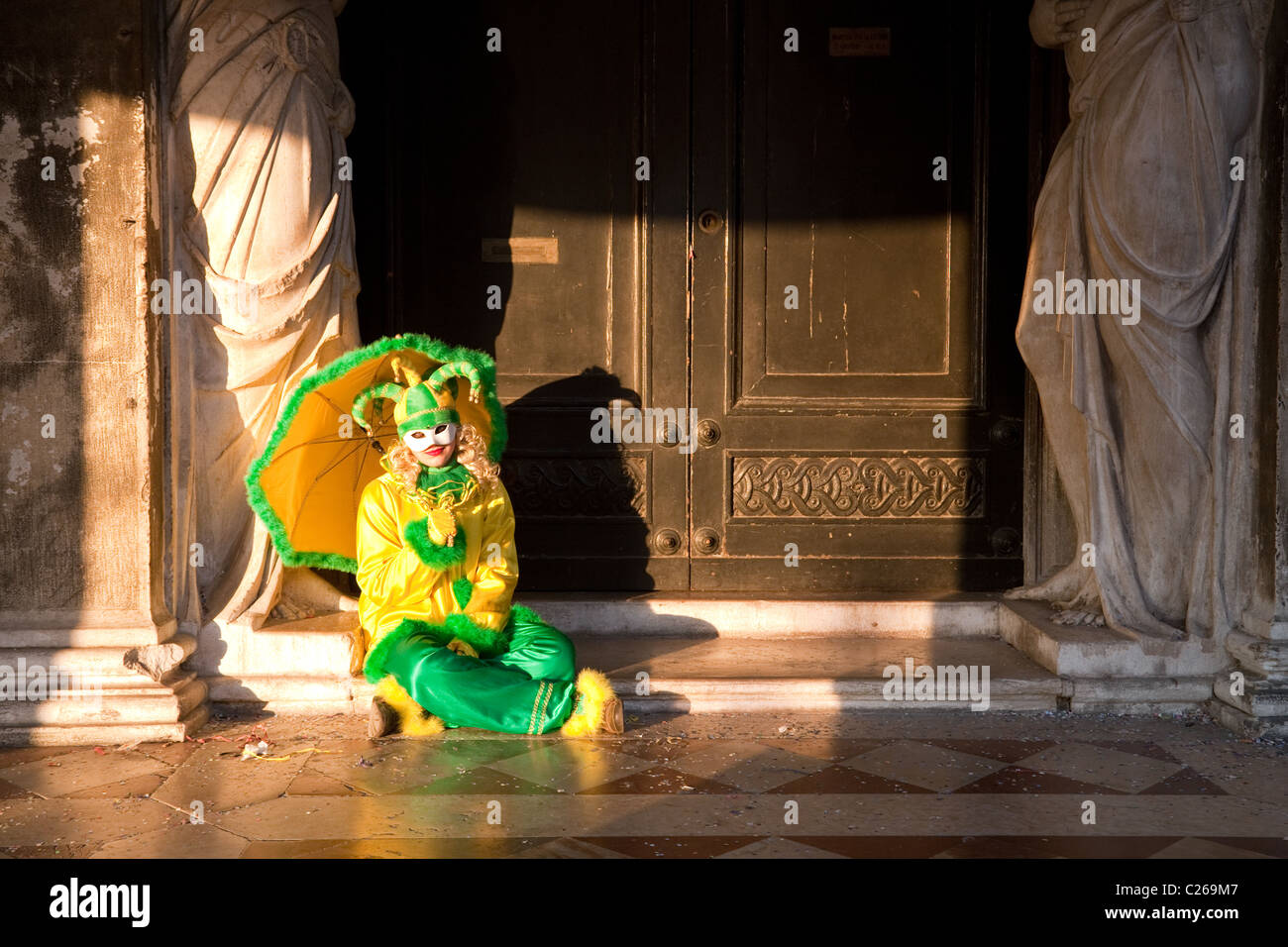 A young woman in clown costume sitting in a doorway, St Marks square, the carnival, Venice, Italy Stock Photo