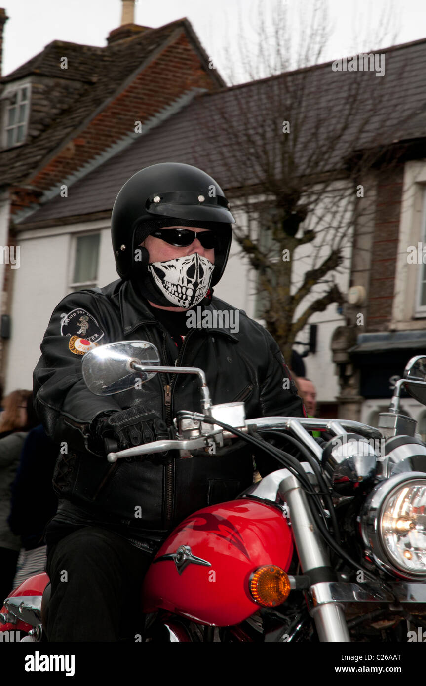 Motorcyclist wearing his black crash helmet and novelty skull face mask rides his motorbike along Wootton Bassett High Street Stock Photo