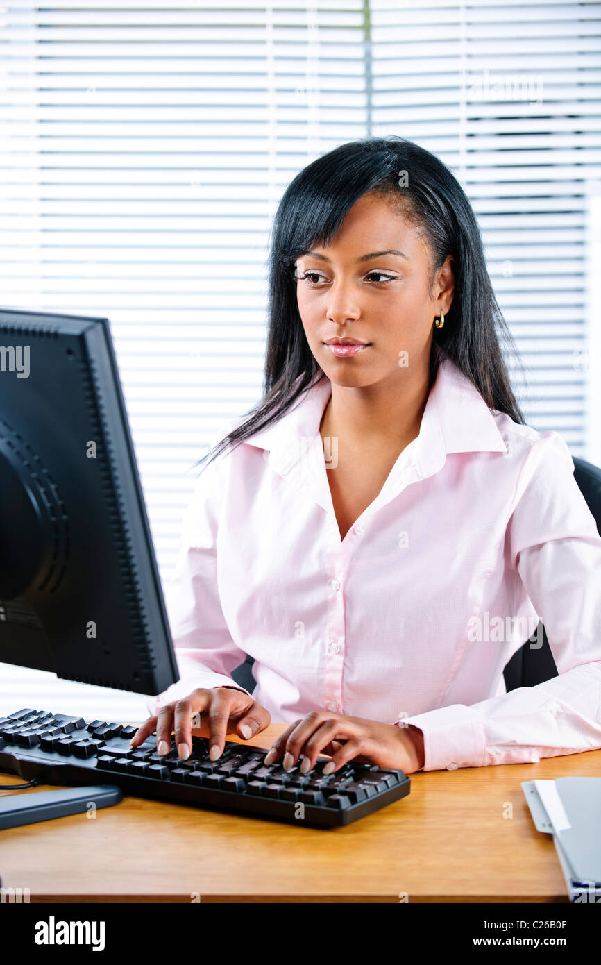 Portrait of serious young black business woman at desk typing on ...