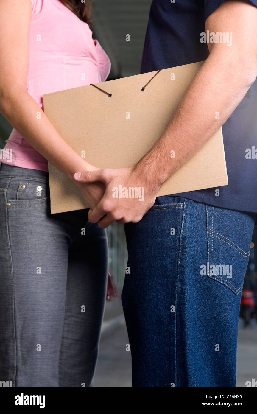 Couple, man, boy, guy, and, woman, lady, hold, holding, each, other’s, hand, holding, a, beige, brown, folder, uni. Stock Photo