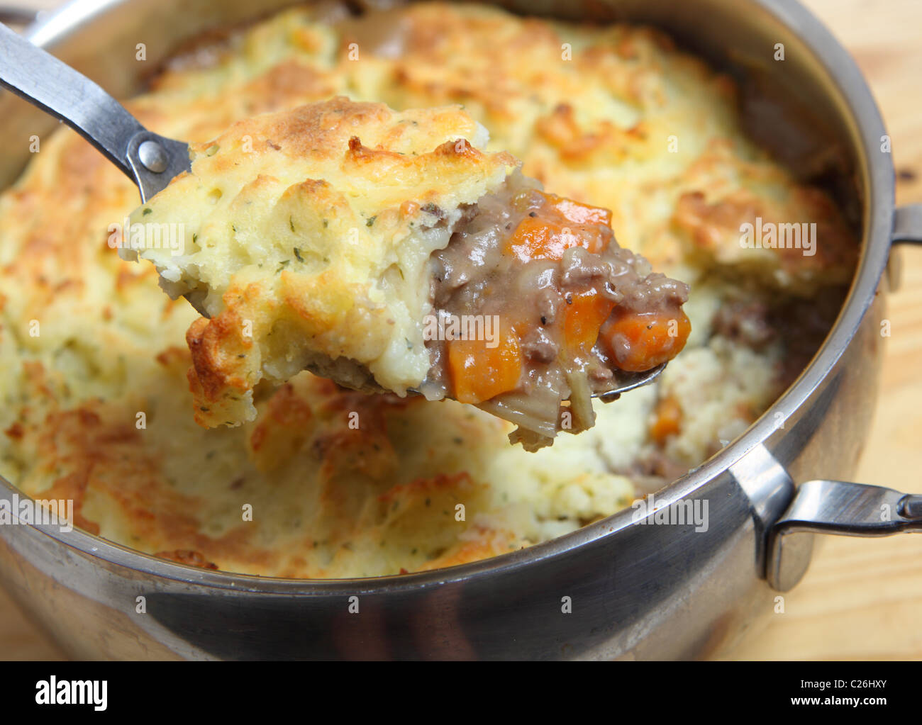 A serving spoon full of shepherd's pie (minced meat and vegetable stew topped with mashed potatoes) over the cooking pot. Stock Photo