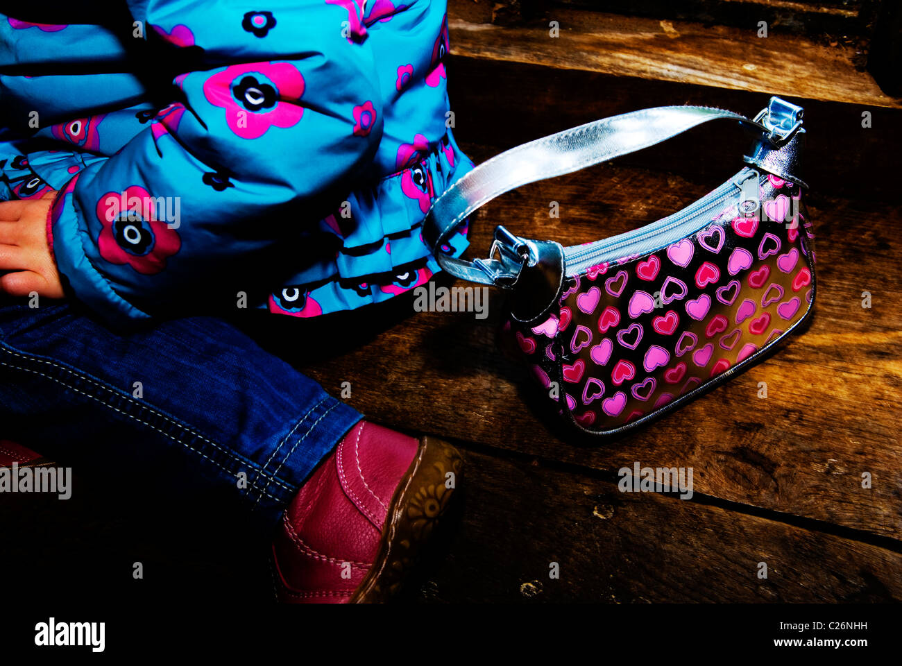 Child sitting on a wooden platform with handbag Stock Photo