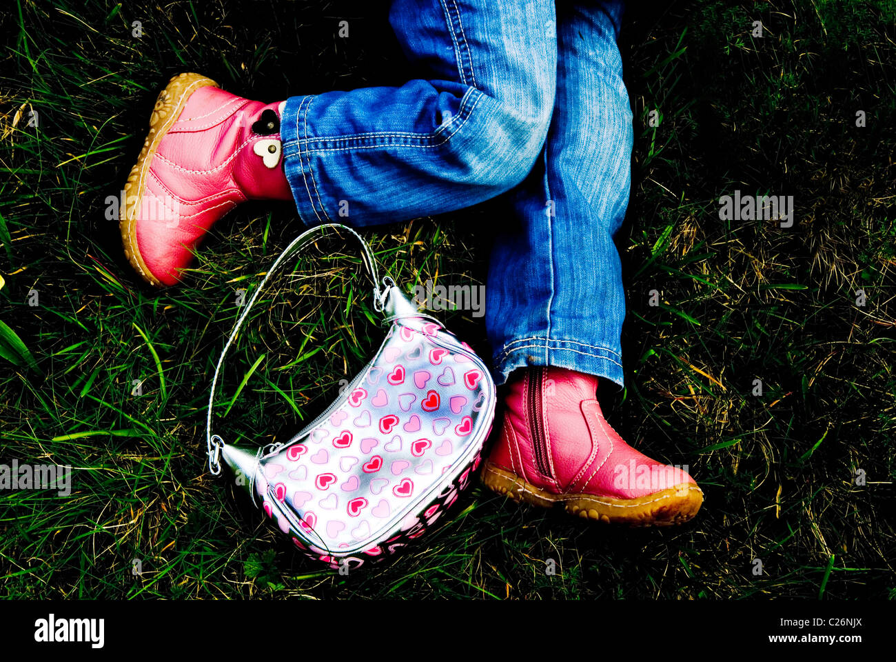 Female child's legs with handbag laying on the grass Stock Photo