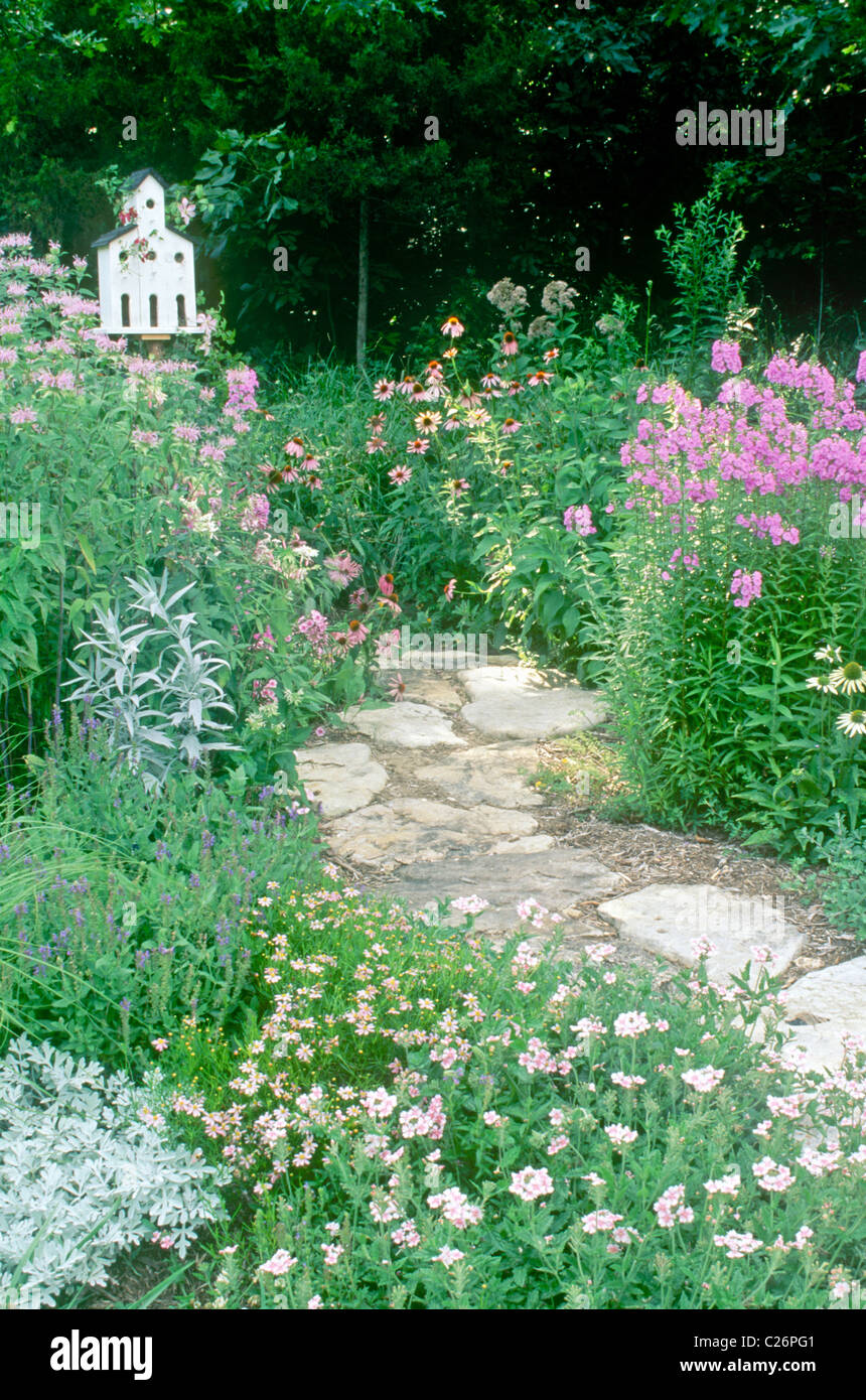 Flagstone path through pastel pinks and lavender garden with church birdhouse entwined with Clematis vine Stock Photo