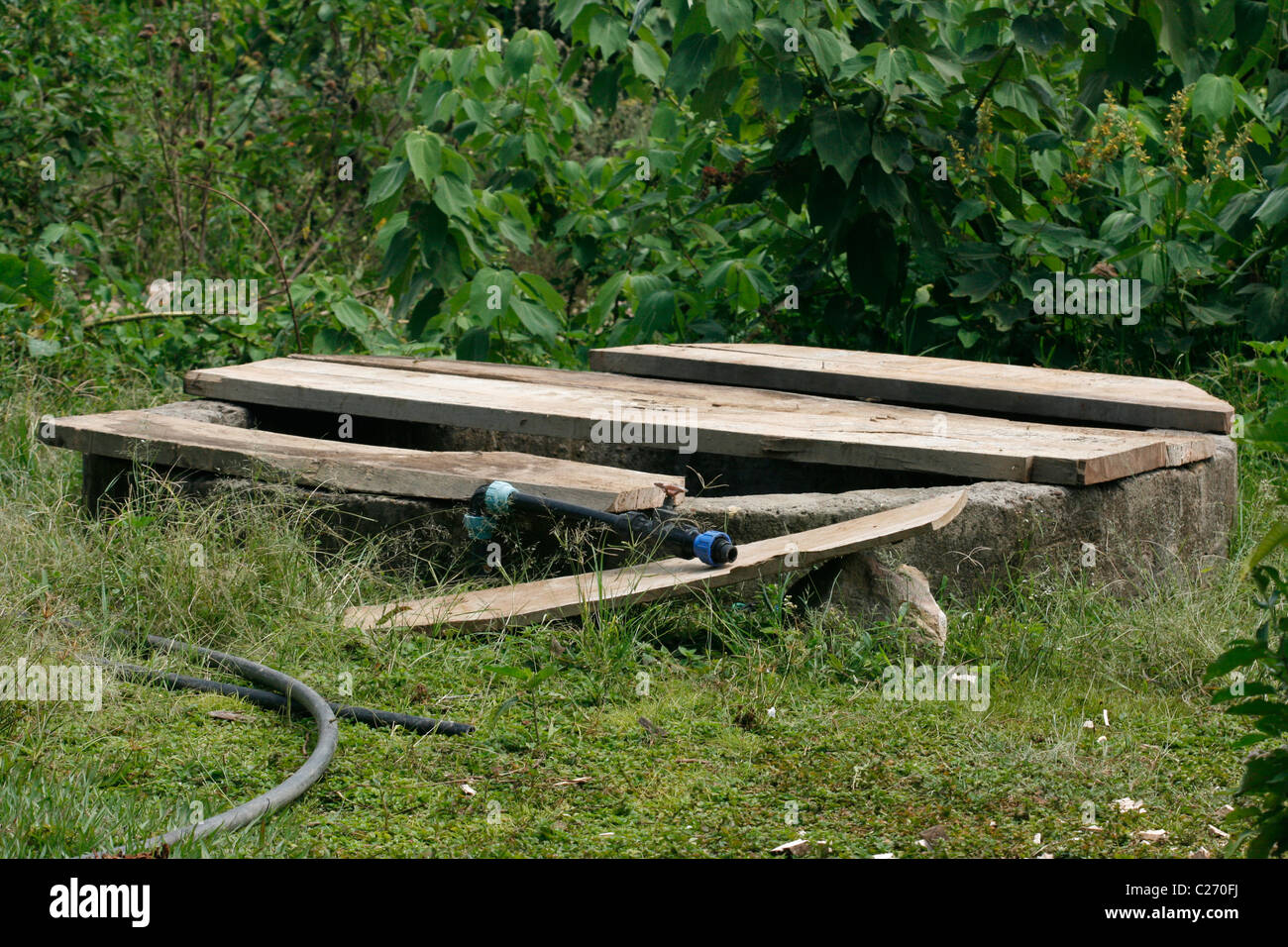 A traditional style water well covered with loose planks. A hose for pumping water lies beside it Stock Photo