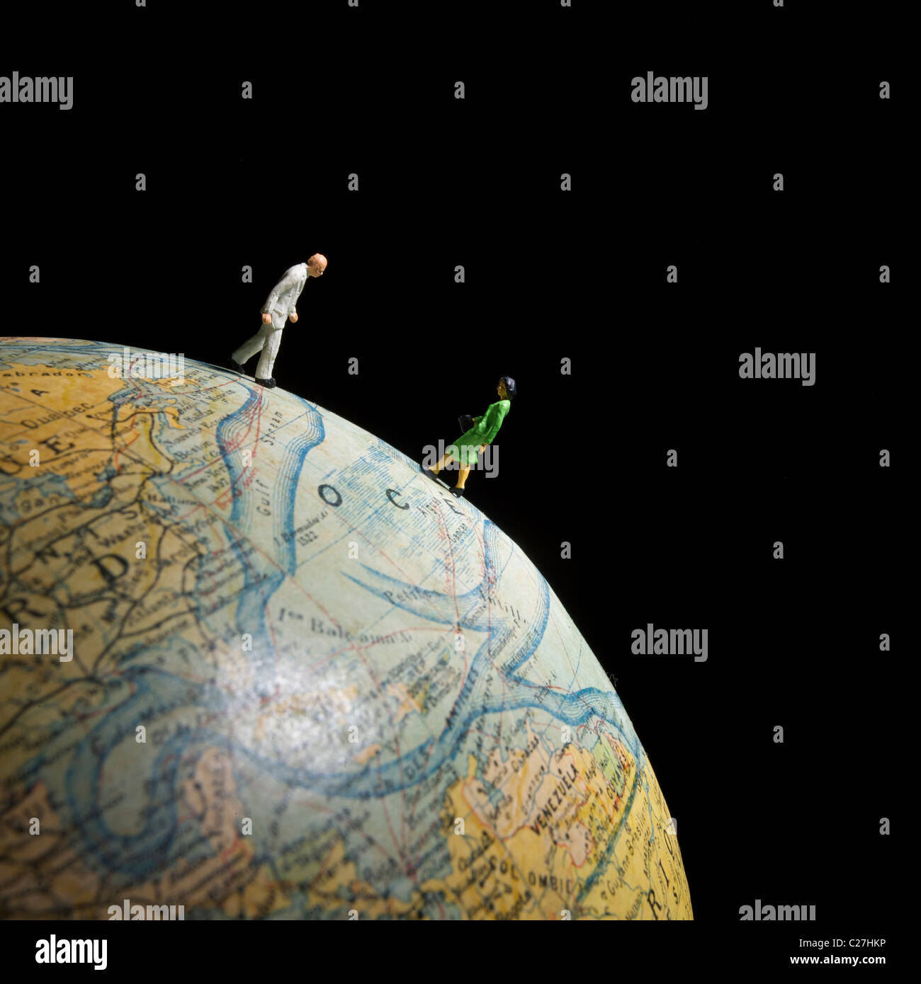 Two miniature figures explore a globe against a black background, highlighting global awareness and curiosity about geography Stock Photo