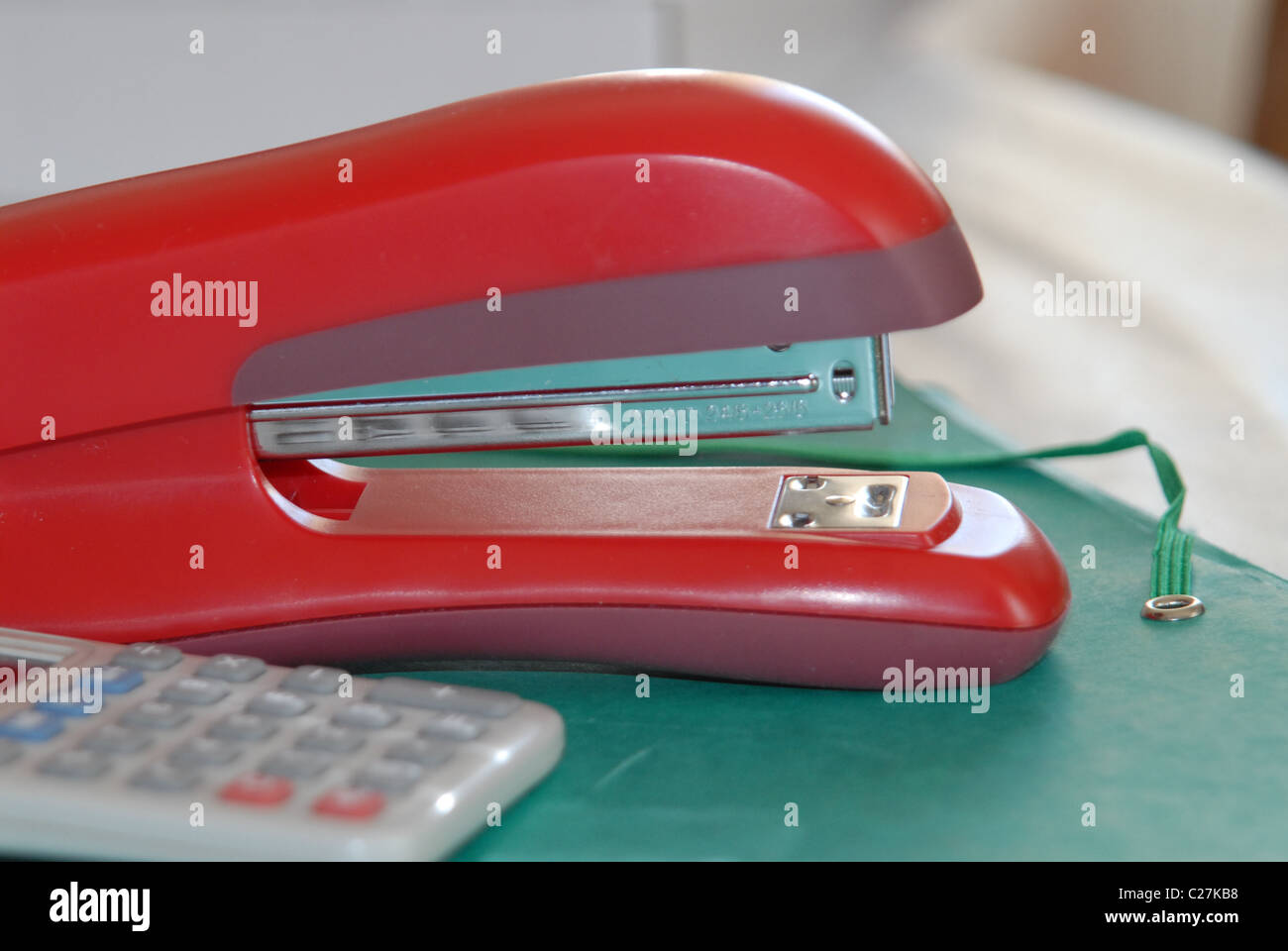 Red stapler, calculator and green file on an office desk. Stock Photo