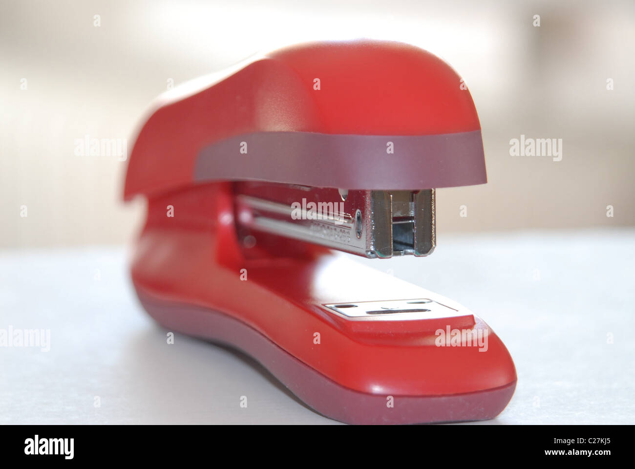 Red stapler on a white desk by a window, front view. Stock Photo