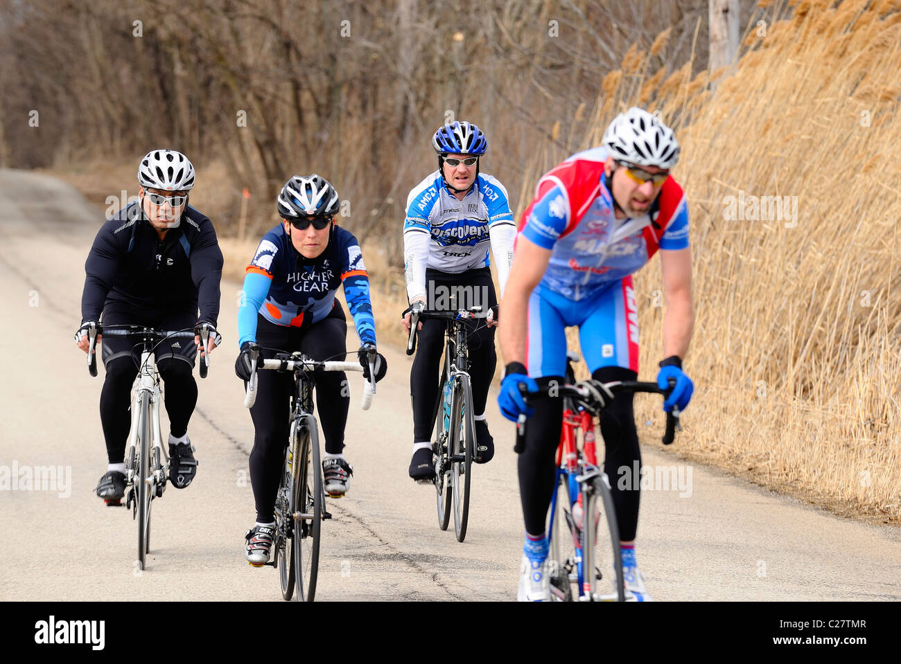 Group of 4 diversified bicyclists pedaling on rural road in spring Stock Photo