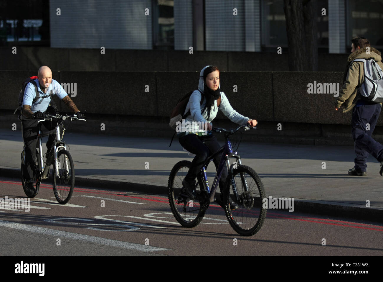 A female cyclist followed by a male cyclist in late afternoon sunshine ...