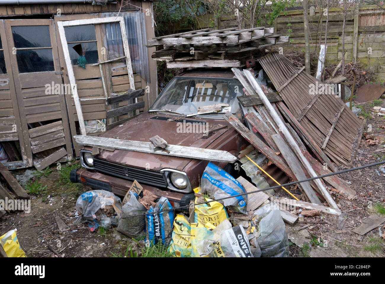 A disused car covered with rubbish abandoned outside a residentual garage. Stock Photo