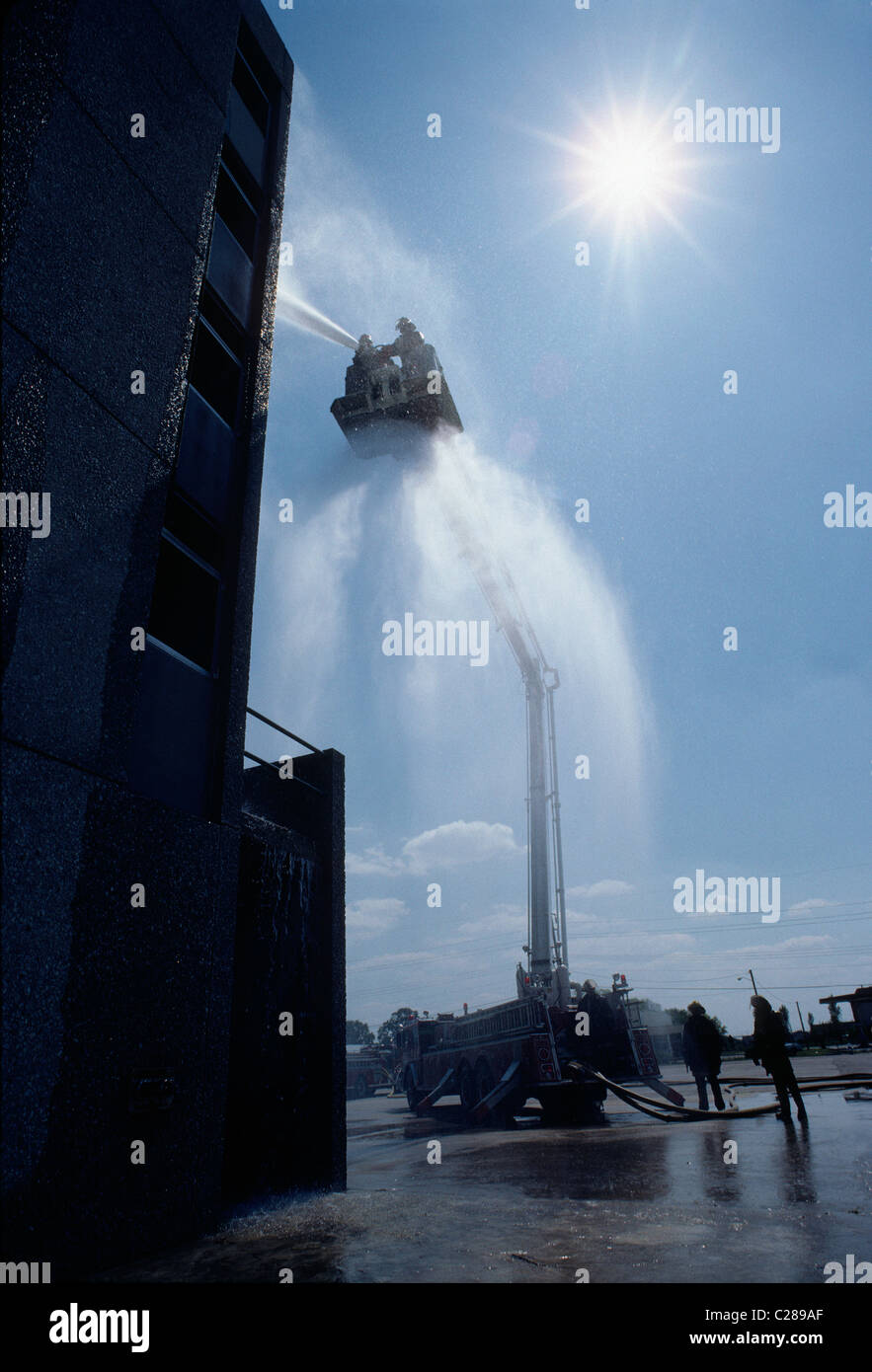Fireman spraying water from a hose mounted on a the ladder bucket of a fire truck Stock Photo
