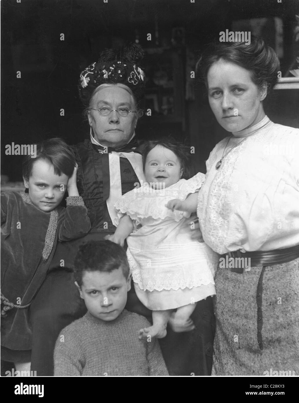 Original Edwardian era glass negative portrait of a respectable Edwardian family. The older woman is a very stern matriarch still dressed in Victorian style clothing with her daughter or daughter in law and her family in the doorway of their home, U.K. circa 1912 Stock Photo