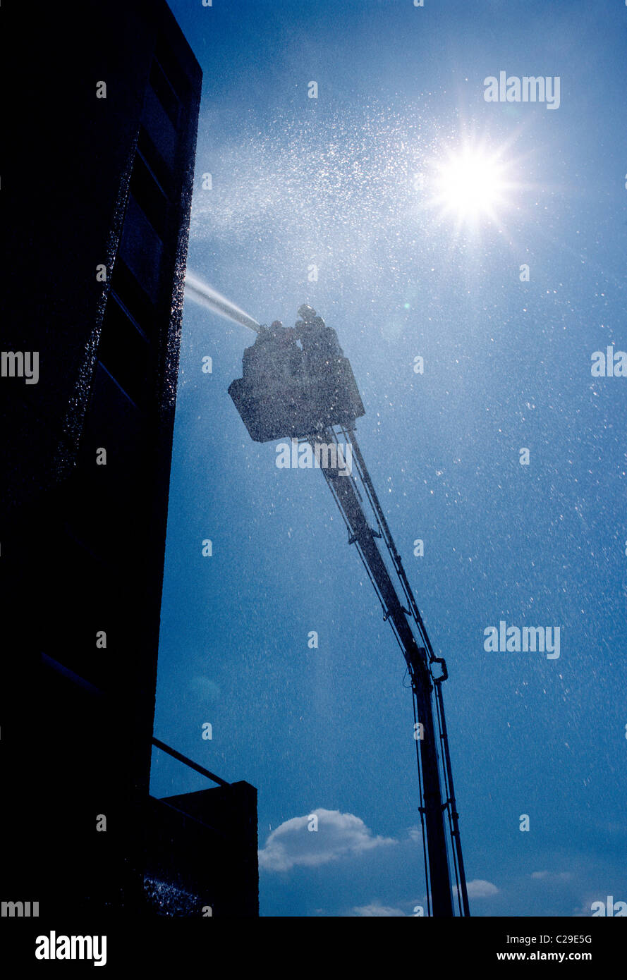 Fireman spraying water from a hose mounted on a the ladder bucket of a fire truck Stock Photo