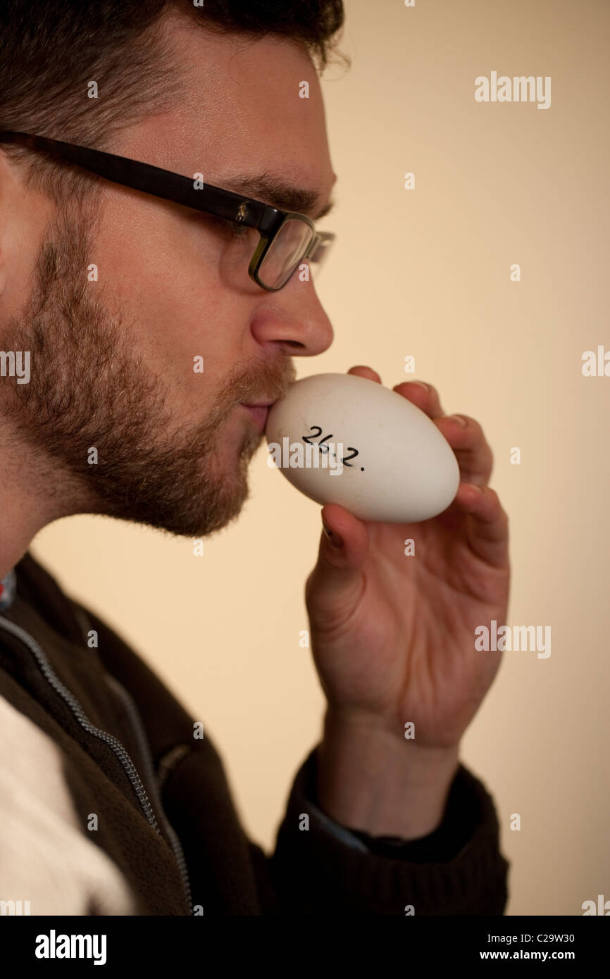 Aviculturist  sensing size of air space within a fertile egg, using his lips. Larger air space indicates near hatching. Stock Photo