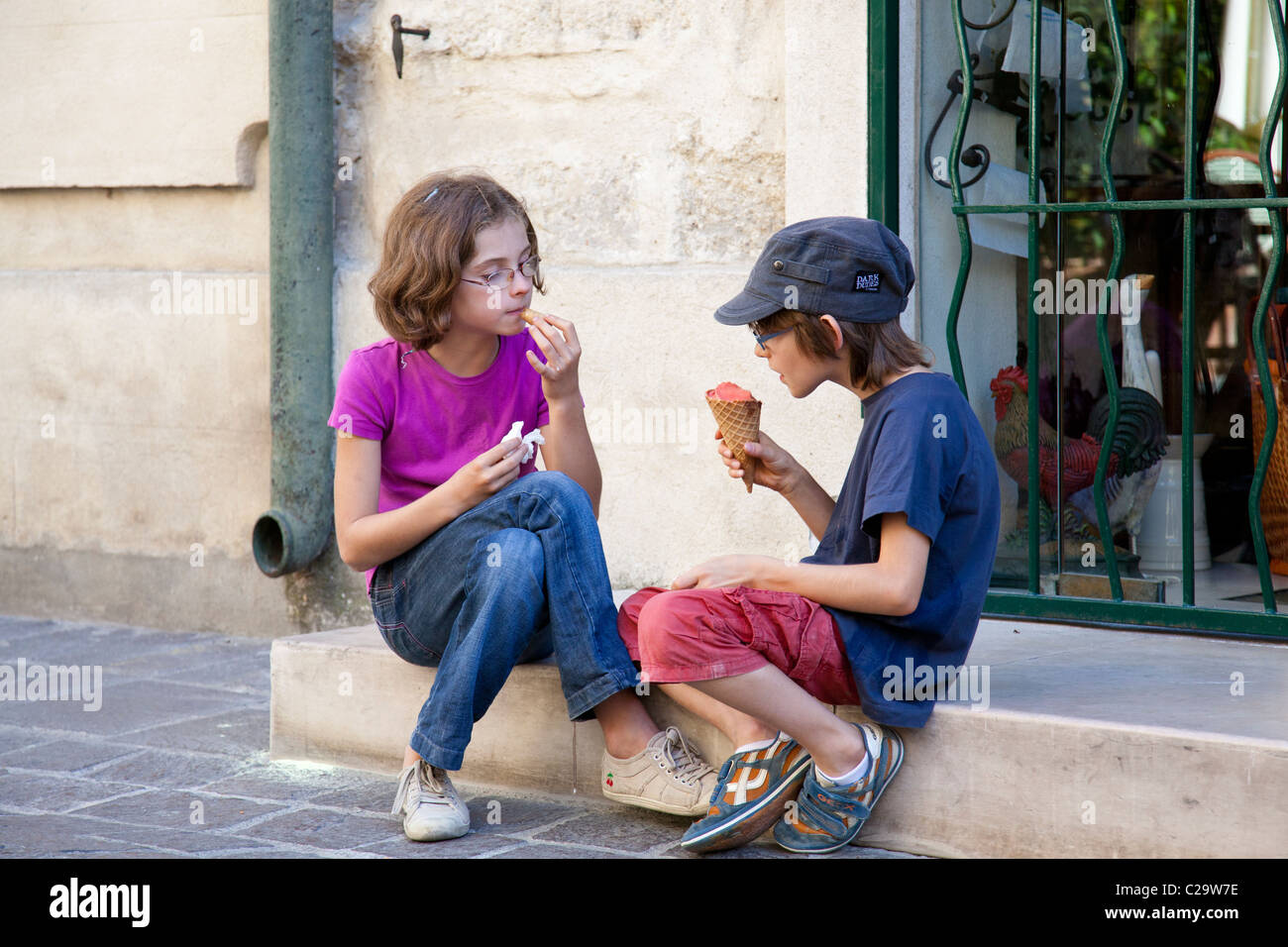 Two children enjoy their ice creams whilst sitting on some shop steps