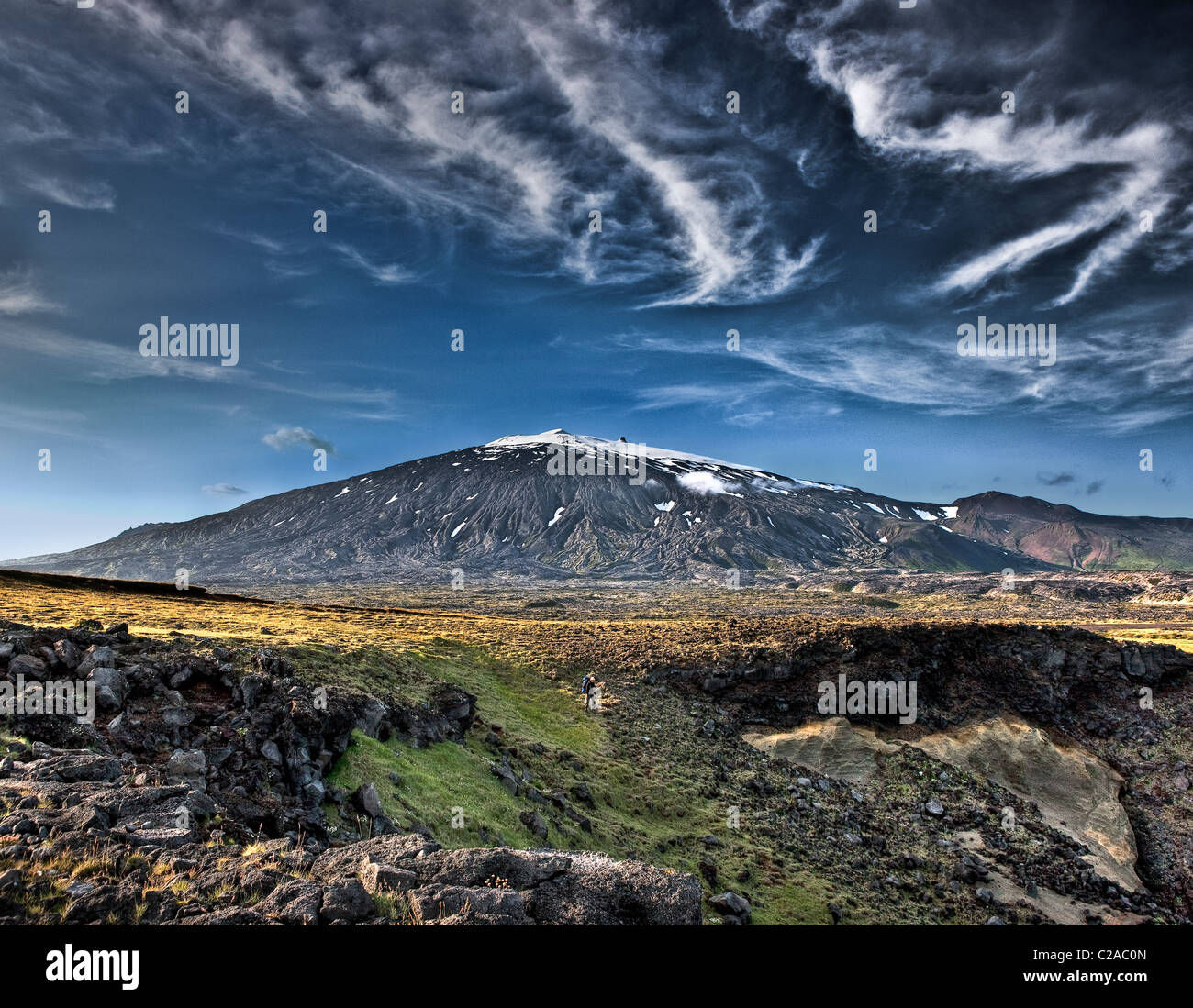 A tourist walking between lava rock and moss with Snaefellsjokull Glacier in background, Iceland Stock Photo