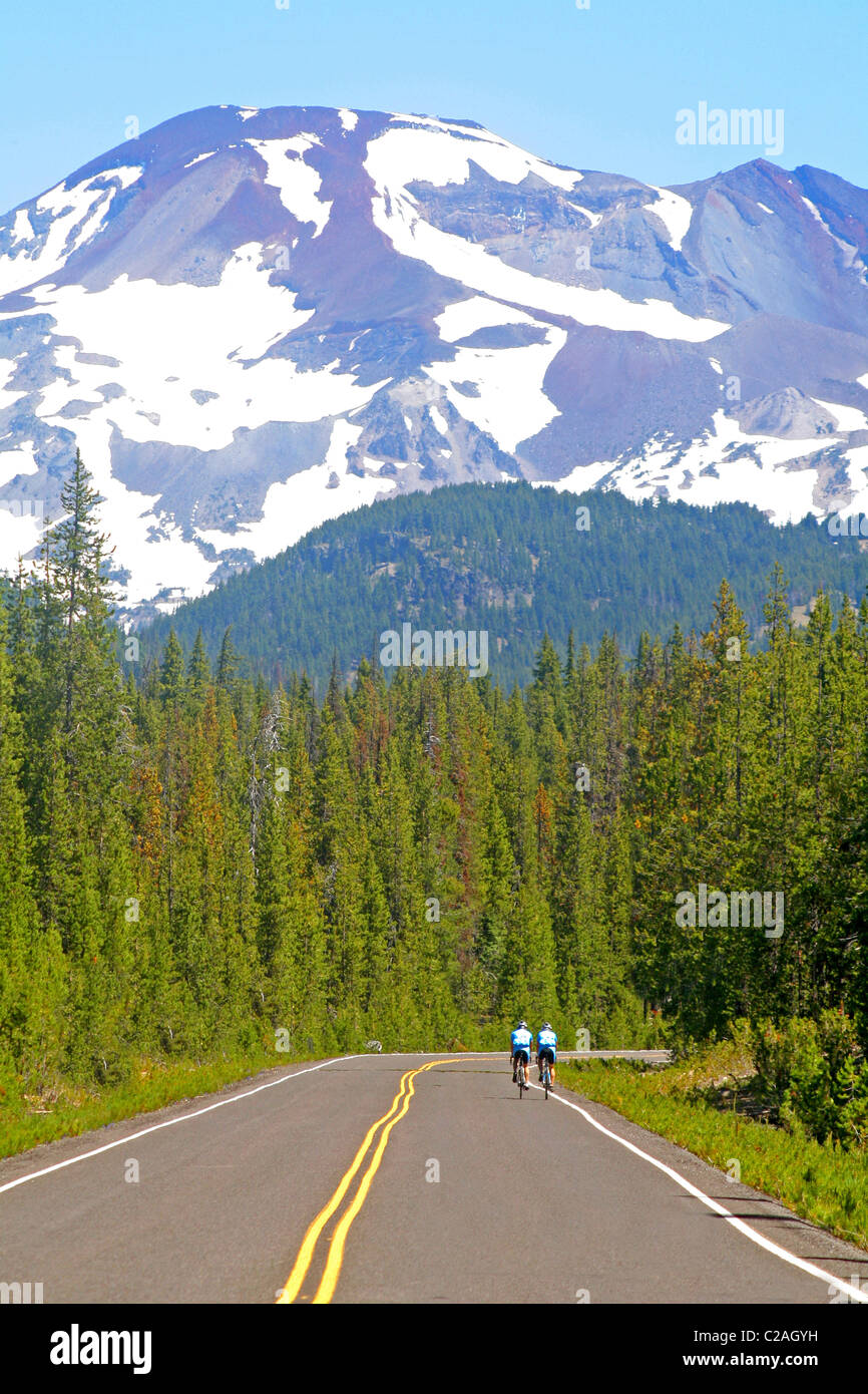 Bicyclists traveling towards The Sisters Mountain above Cascade Lakes National Scenic Byway Oregon Stock Photo
