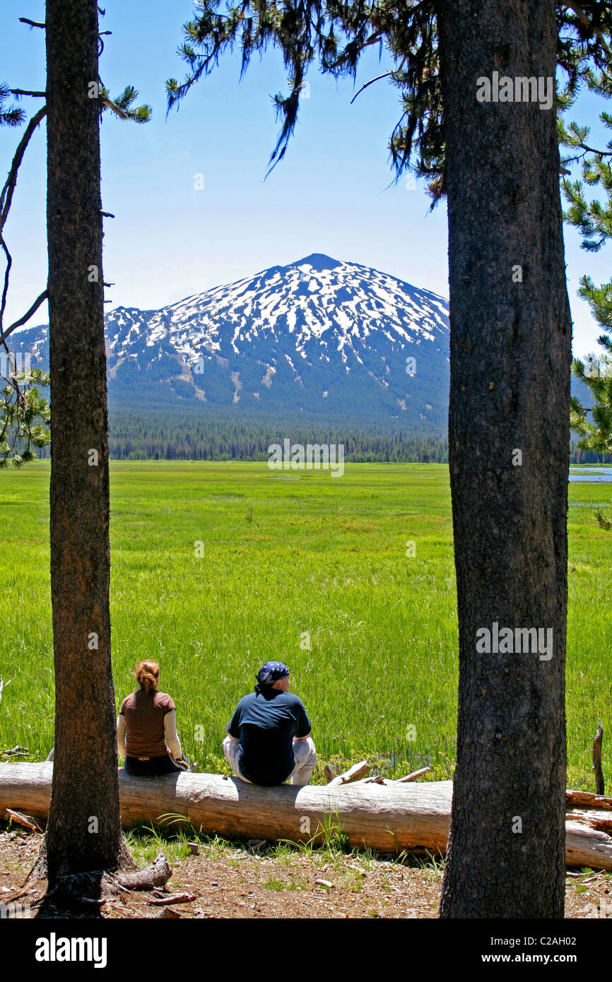 Couple sitting at  Sparks Lake near Mt. Bachelor on Cascade Lakes National Scenic Byway Oregon Stock Photo