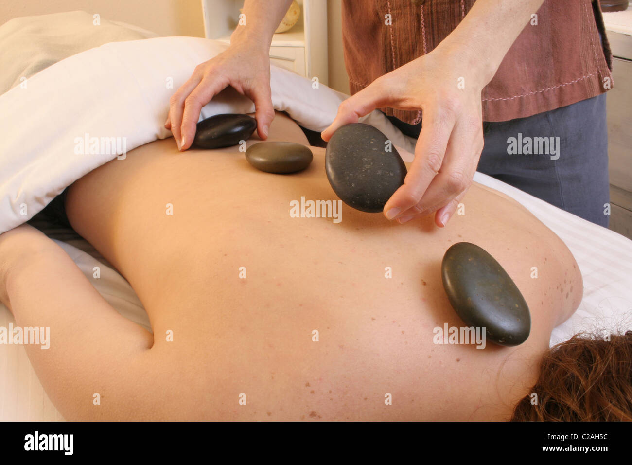 Released health spa massage therapist places heated stones on back Stock Photo