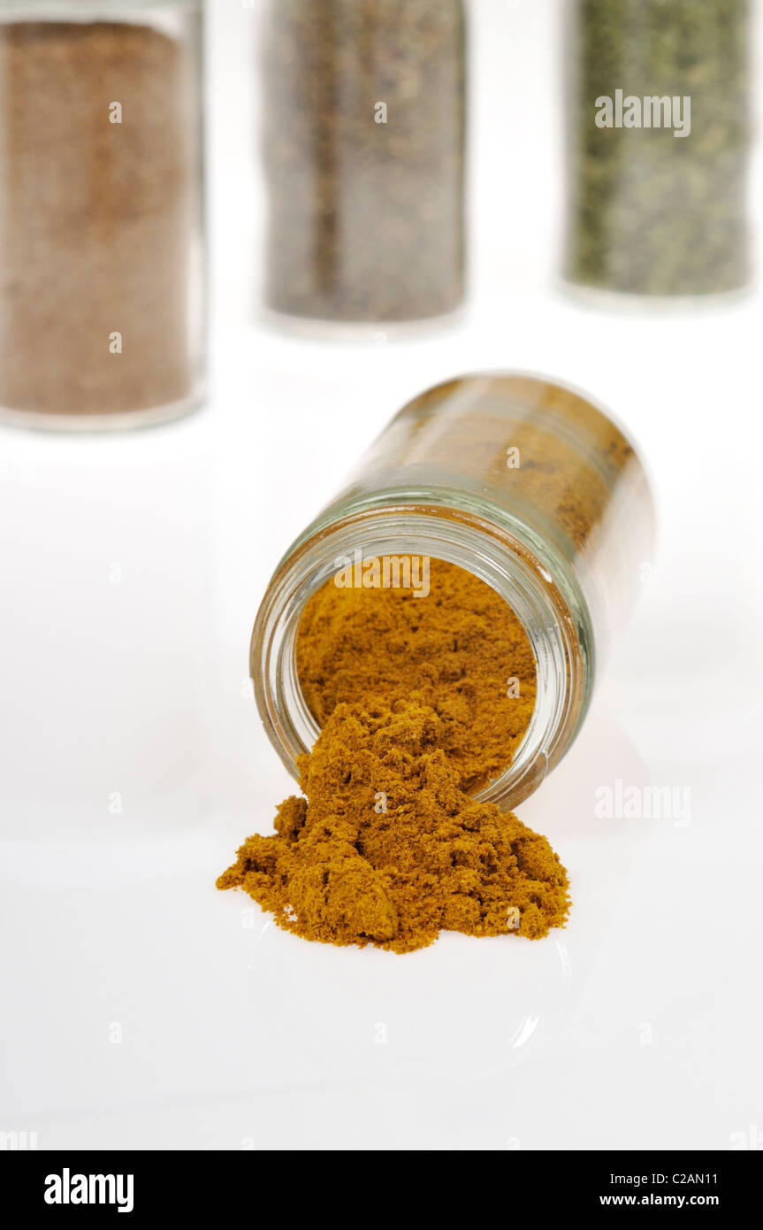Bottle of the spice curry open and on it side with curry spilling out and herb and spice bottles in background on white. Stock Photo