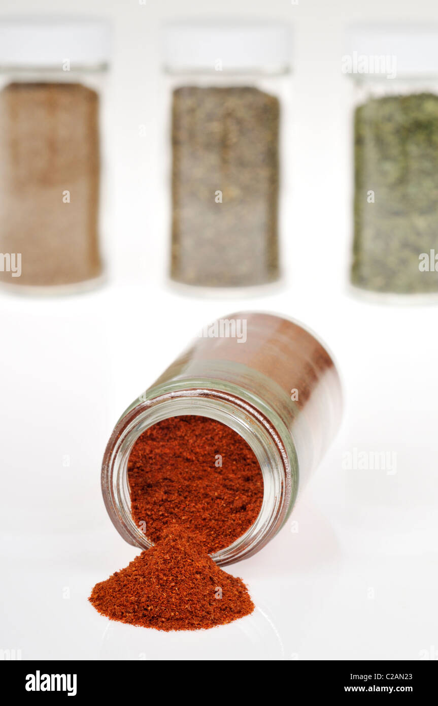 Bottle of spice cayenne pepper open and on it side with cayenne pepper spilling out and herb and spice bottles in background. Stock Photo