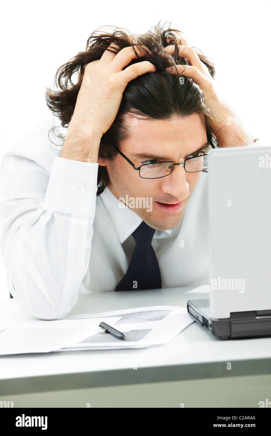 Portrait of serious businessman with glasses touching head in front of laptop Stock Photo